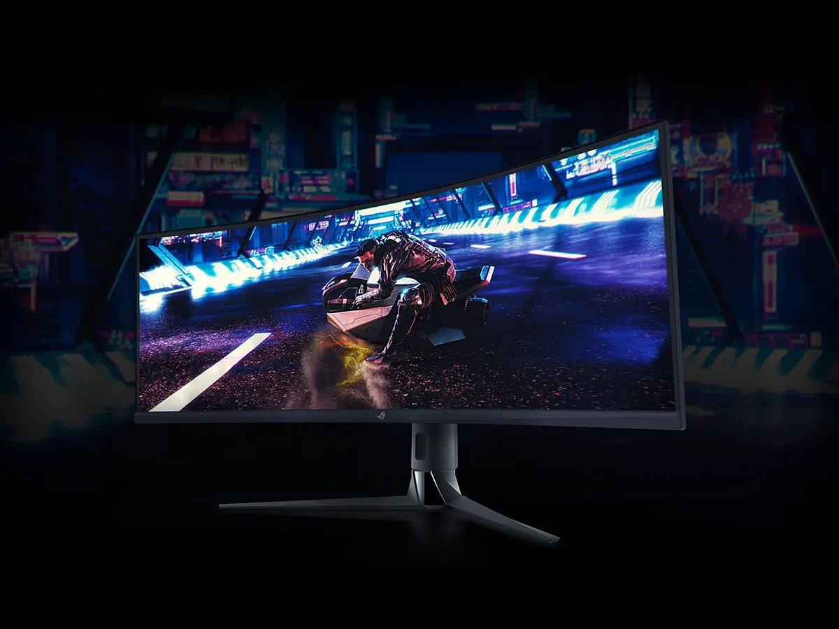 A large curved monitor displays a futuristic racing game. A motorcyclist speeds through a neon-lit city. A keyboard and mouse are in front, set against a dark blue backdrop.