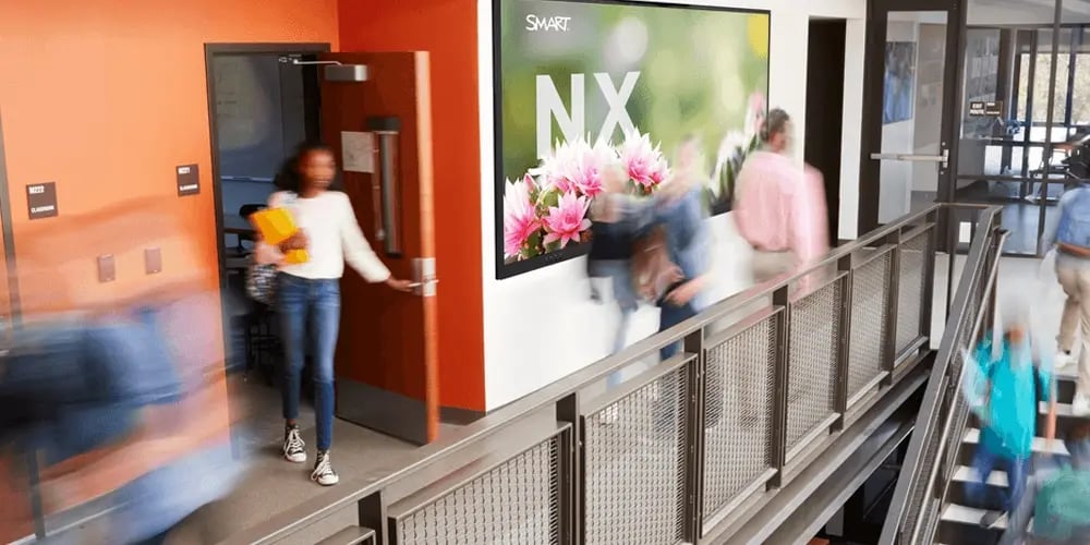 Blurred students walk through a bright school hallway. A large floral poster reads 