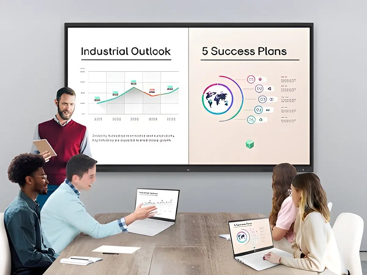 A group of diverse individuals sits around a table with laptops, attentively viewing a presentation. The screen displays a graph titled 
