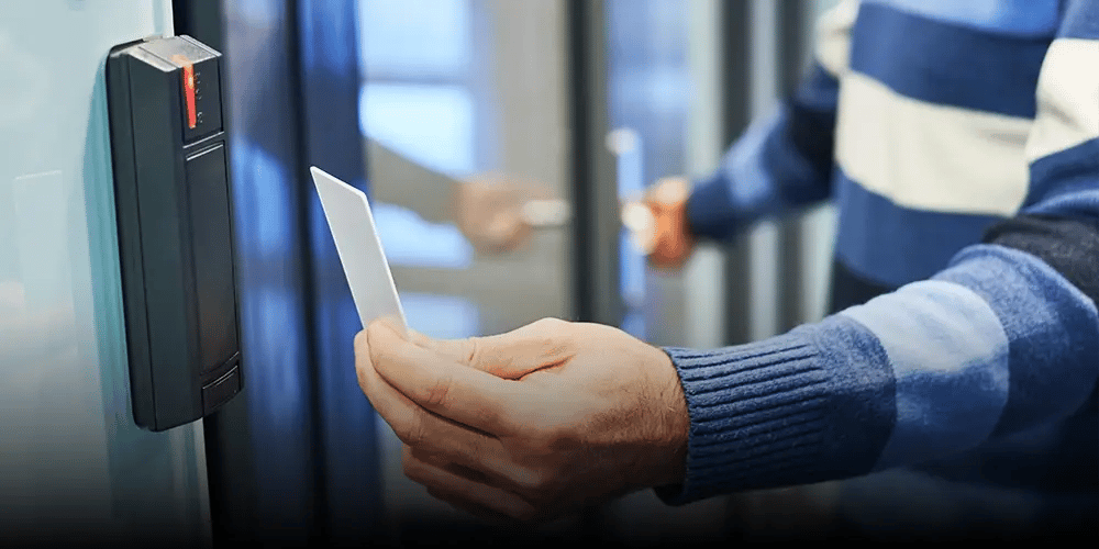 A person holds a key card up to an access control reader next to a glass door to gain entry.