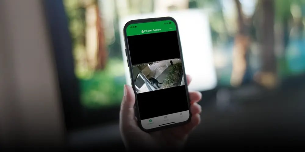 A hand holds a smartphone displaying a security camera feed through the 