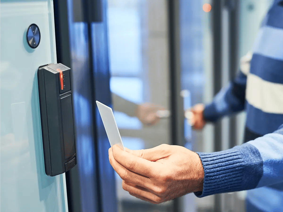 A person holds a key card up to an access control reader next to a glass door to gain entry.