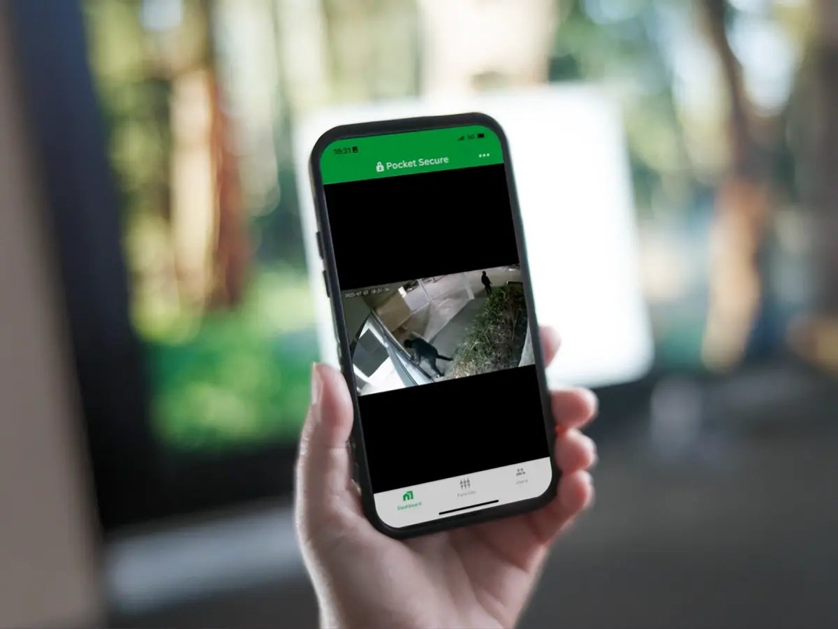 A hand holds a smartphone displaying a security camera feed through the 