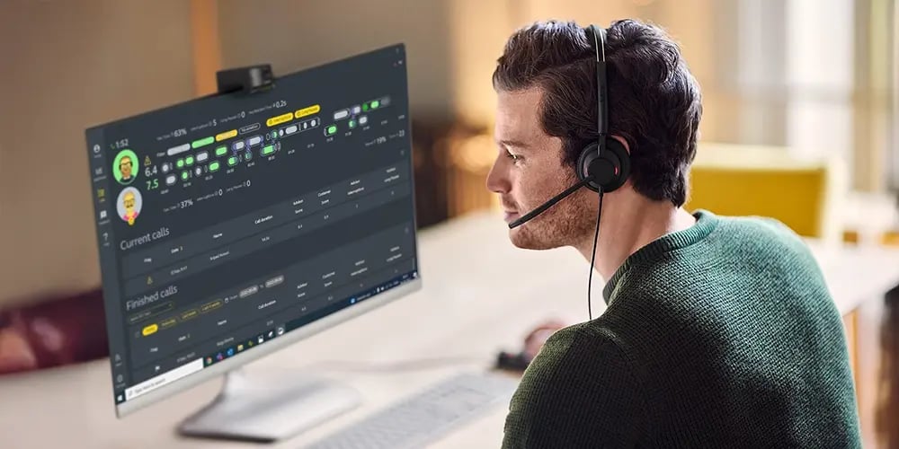 A man with a headset works at a computer displaying call software. The screen shows detailed call analytics. The setting is a bright office space.