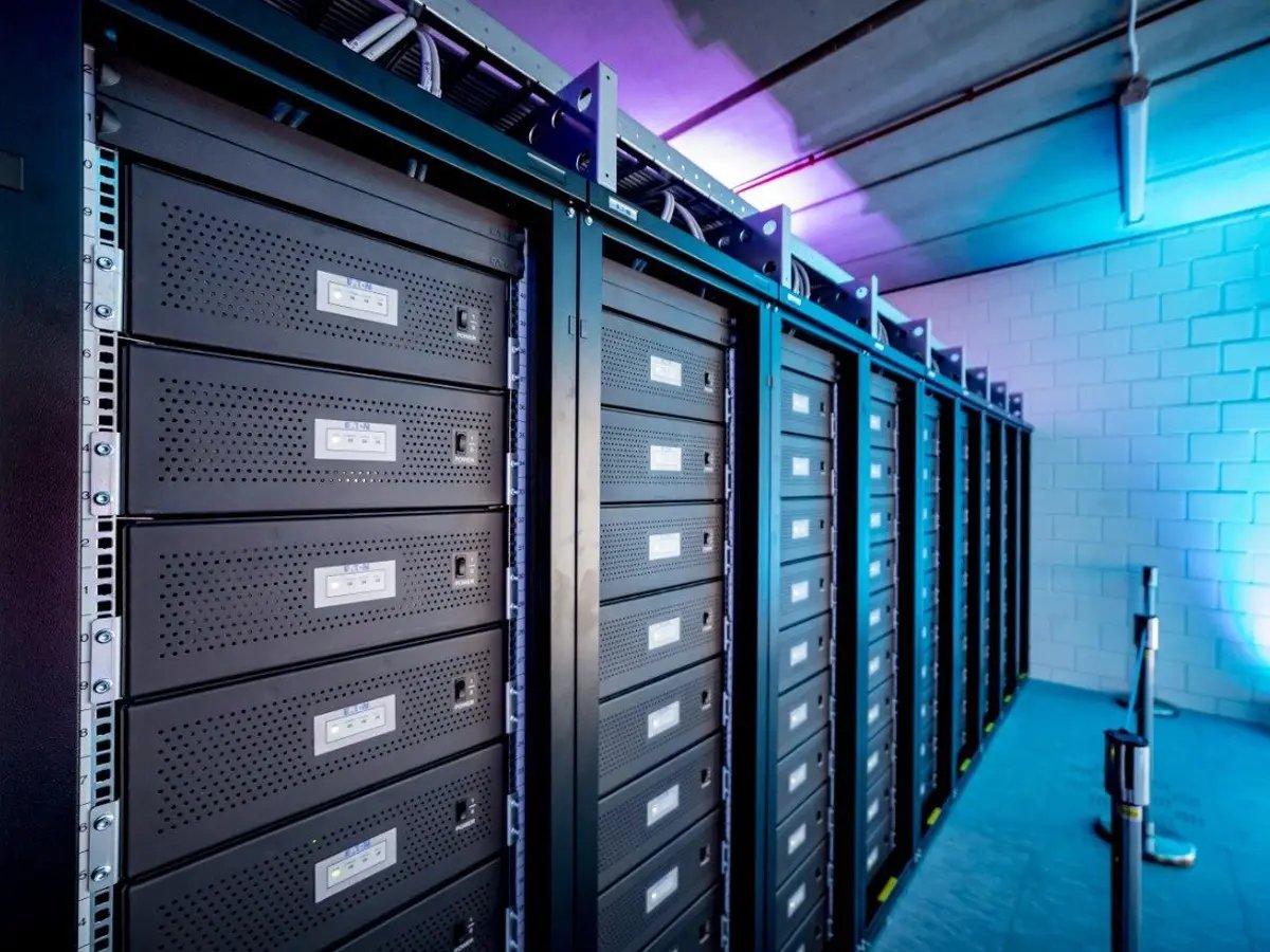 A row of black server racks in a data center with blue and purple ambient lighting, creating a modern and high-tech atmosphere.