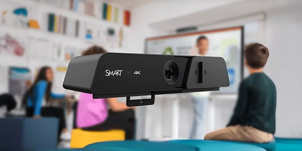 4K smart camera in focus with a blurred classroom setting in the background, featuring students and a teacher at a whiteboard, indicating a tech-enhanced learning environment.