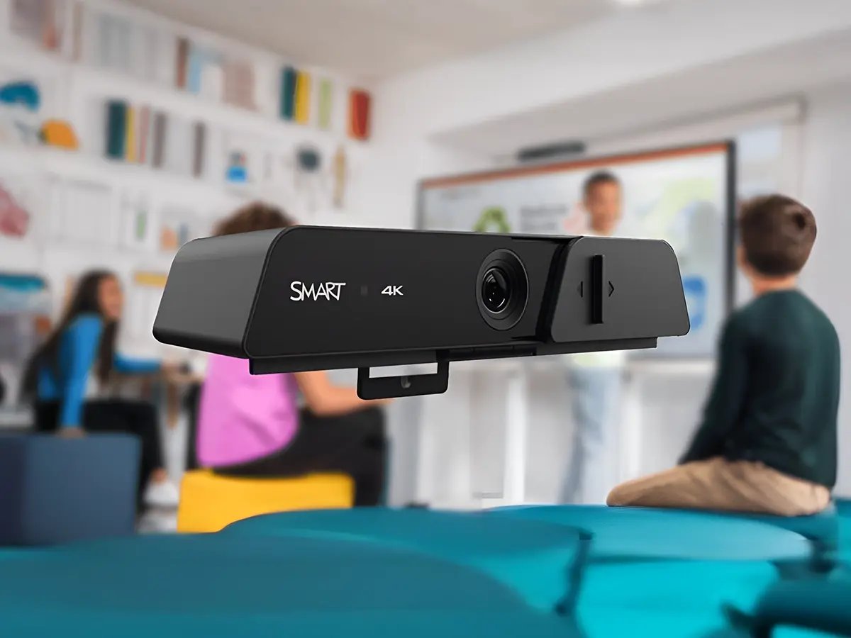 4K smart camera in focus with a blurred classroom setting in the background, featuring students and a teacher at a whiteboard, indicating a tech-enhanced learning environment.