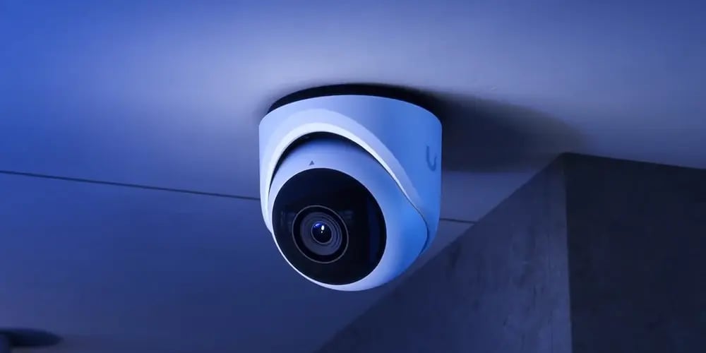 A sleek, modern security camera is mounted on a ceiling, illuminated by blue lighting. It conveys a sense of surveillance and protection.