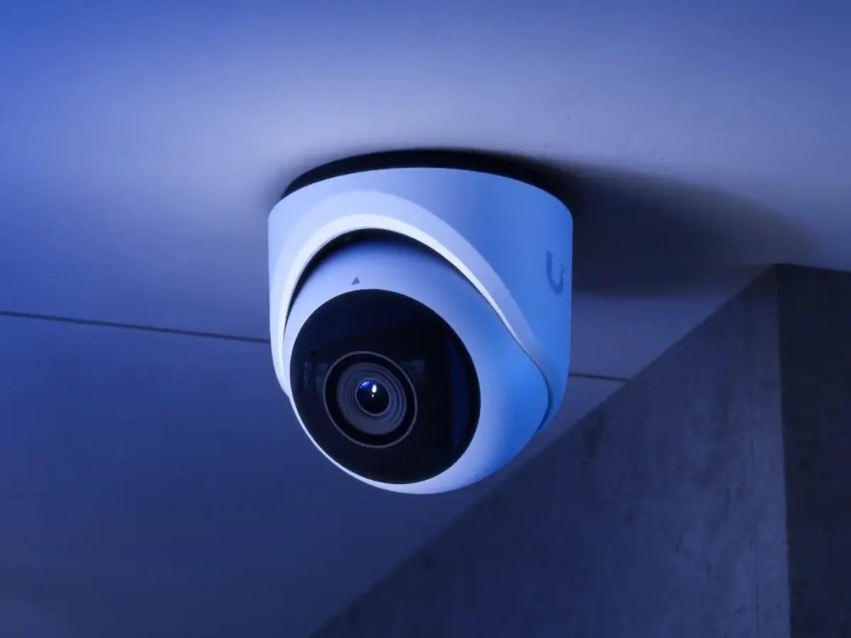 A sleek, modern security camera is mounted on a ceiling, illuminated by blue lighting. It conveys a sense of surveillance and protection.