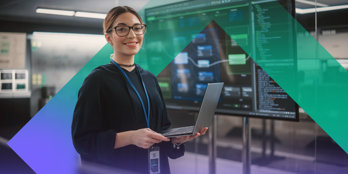 Person holding a laptop in front of large screens displaying data and system interfaces.