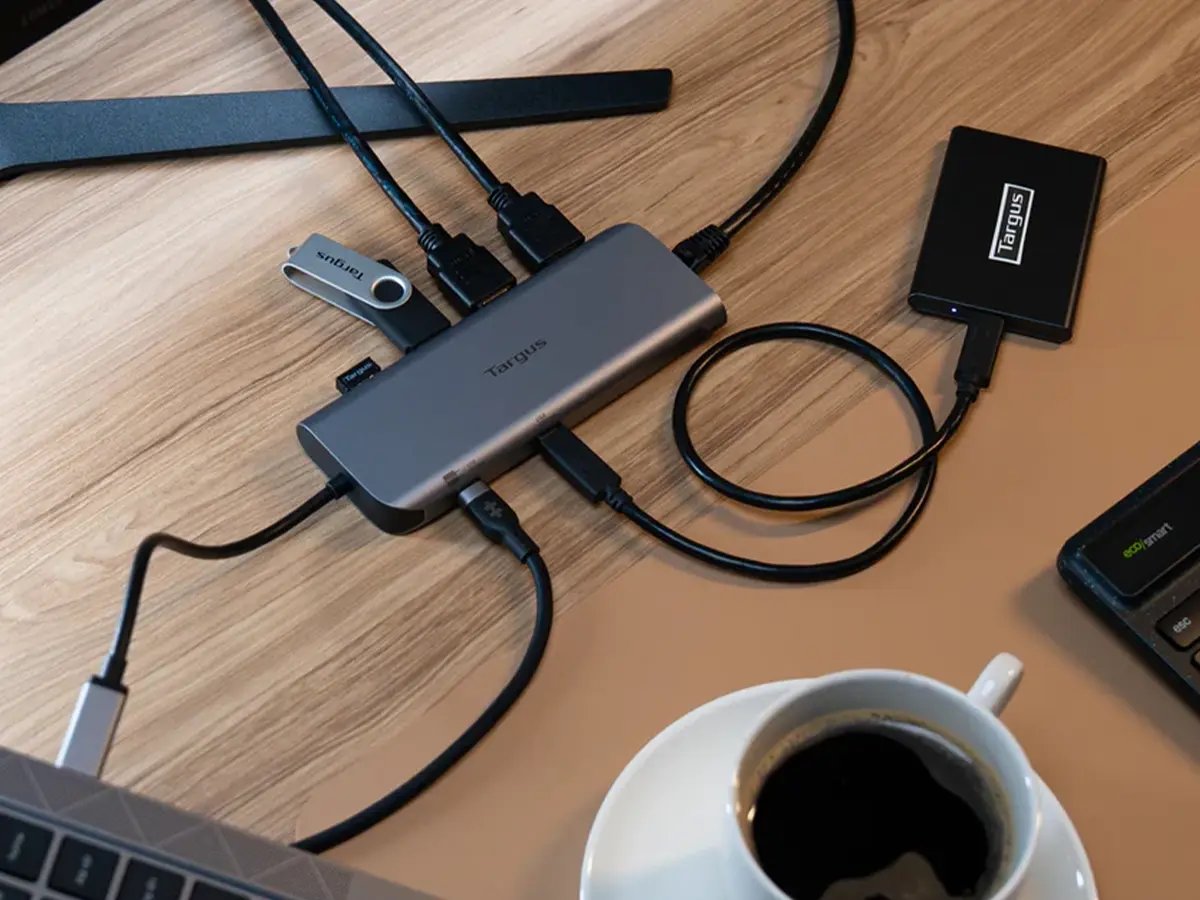A desk setup with a Targus USB hub connected to multiple devices, including cables, a flash drive, an external drive, and a coffee cup nearby.
