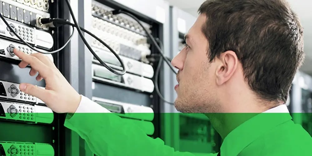 Person adjusting equipment in a server rack with multiple network and security devices, representing security monitoring and system management.
