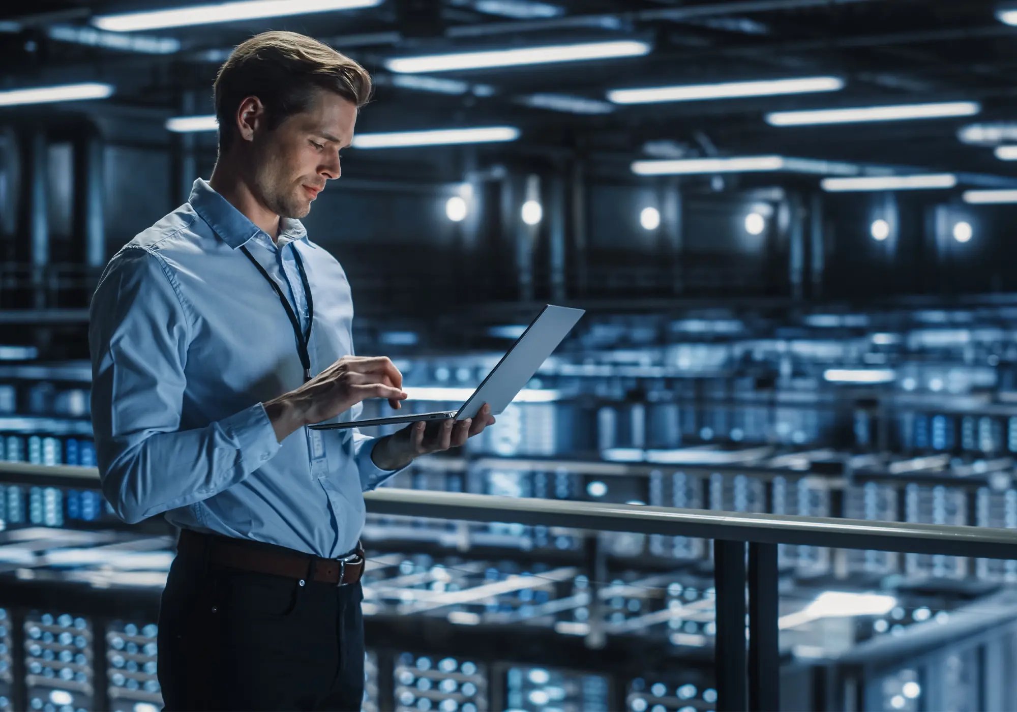 Person using a laptop in a large, modern data center with rows of illuminated server racks in the background.