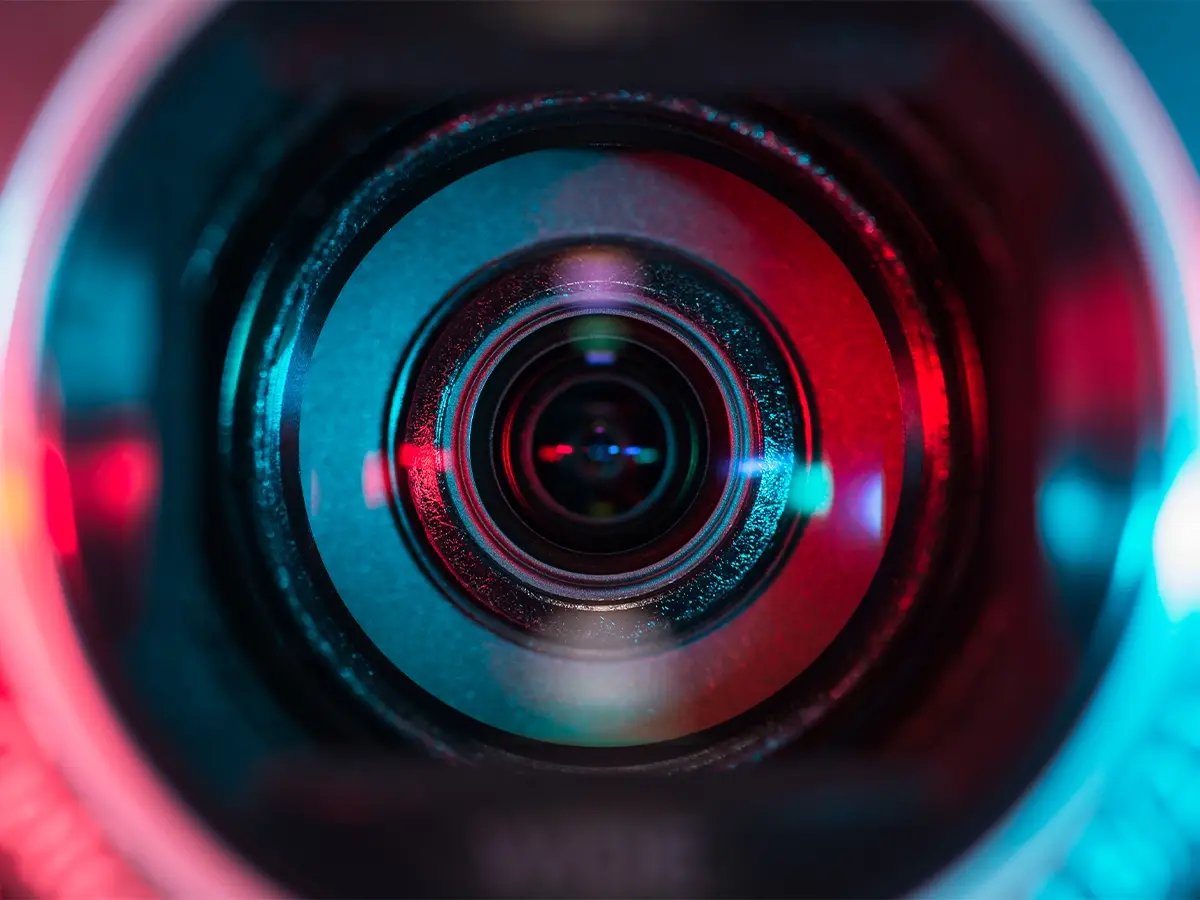 Close-up view of a camera lens with vibrant red and blue lighting reflections, symbolizing monitoring and surveillance technology.