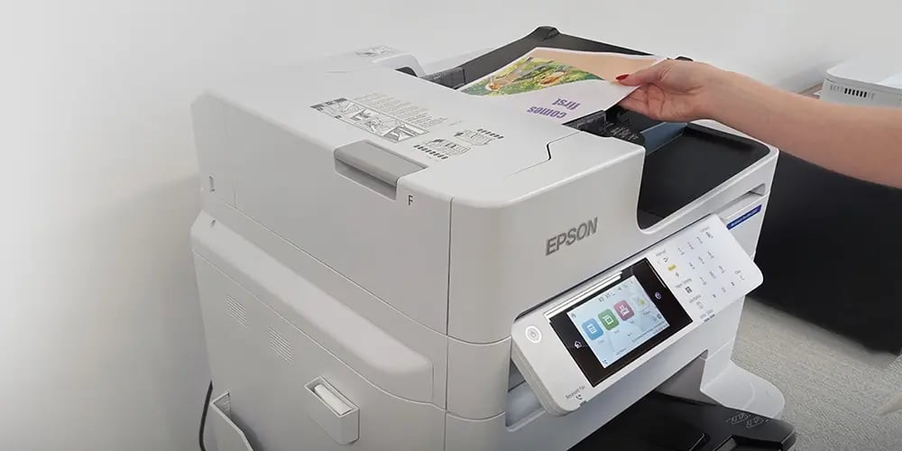 A person placing a printed sheet into an Epson multifunction printer with a touchscreen control panel