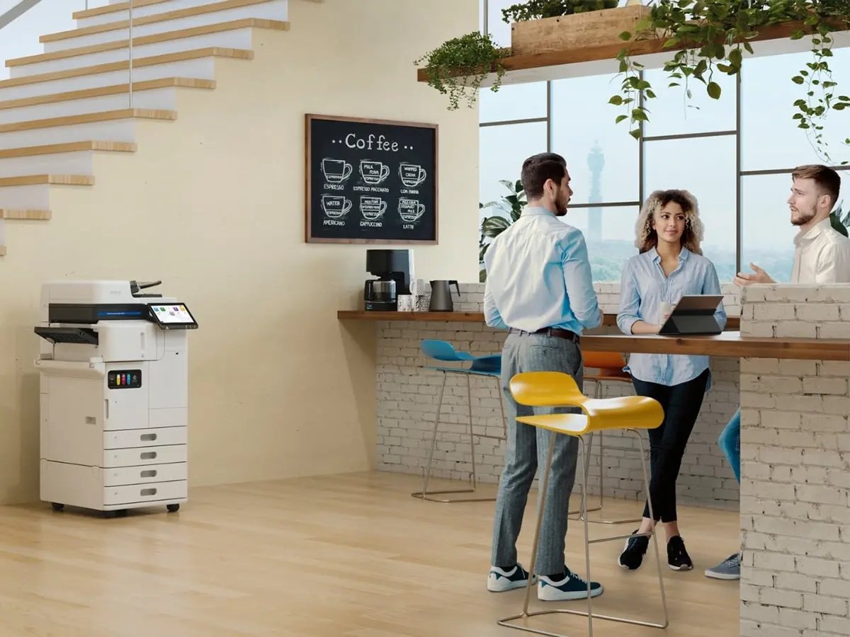 Epson multifunction printer positioned near a coffee bar area with stools and a chalkboard menu in a modern office setting.