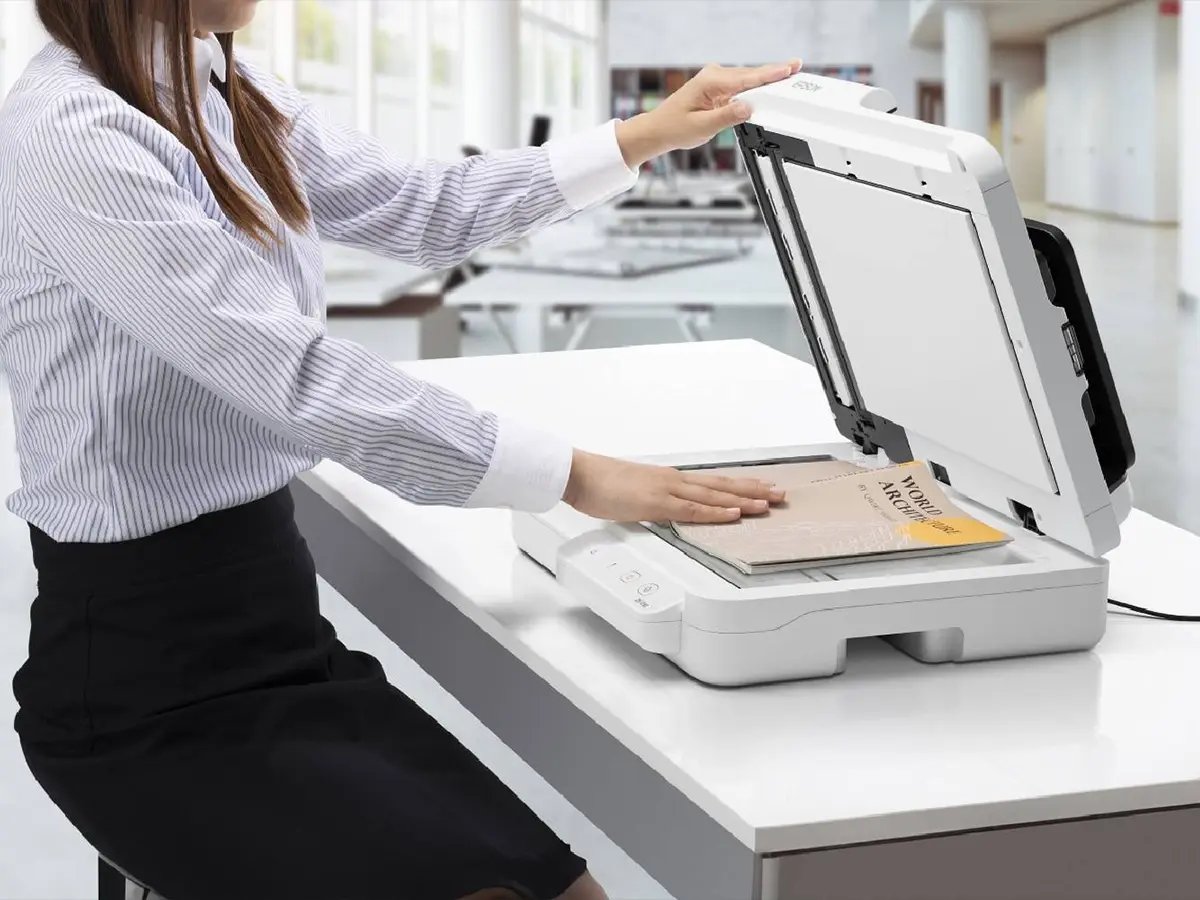 Person placing a document on an Epson flatbed scanner in a modern office environment.