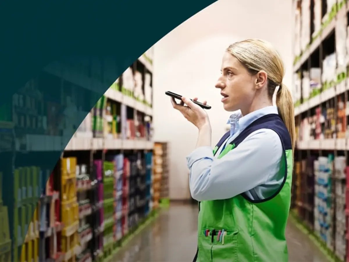 Frontline worker in a green vest using a smartphone for communication while standing in a store aisle.
