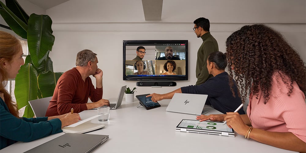 A team of 5 people with their HP notebooks in a meeting room, facing a screen on a wall, with people on a conference call