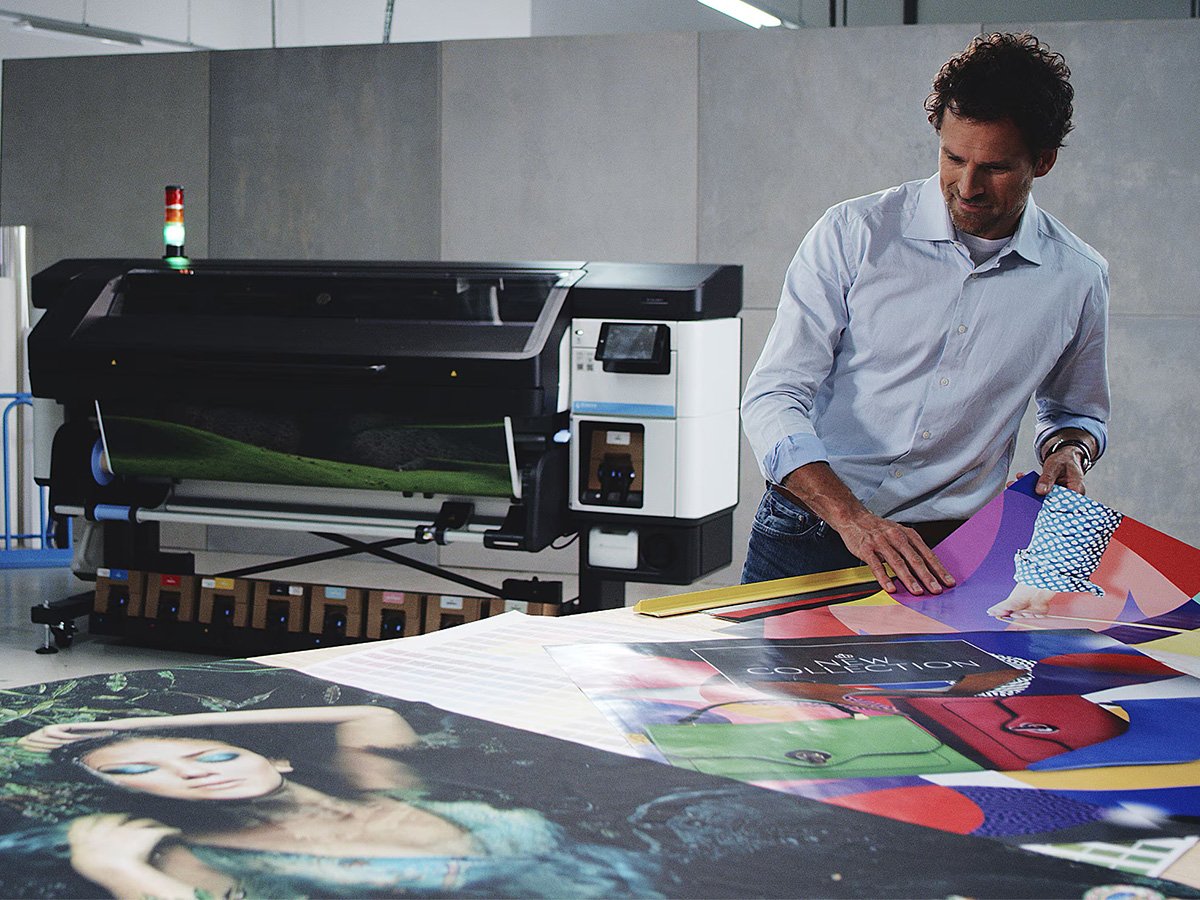 A person in a professional print workshop is laying out A0 posters on a table in front of a HP large-format printer