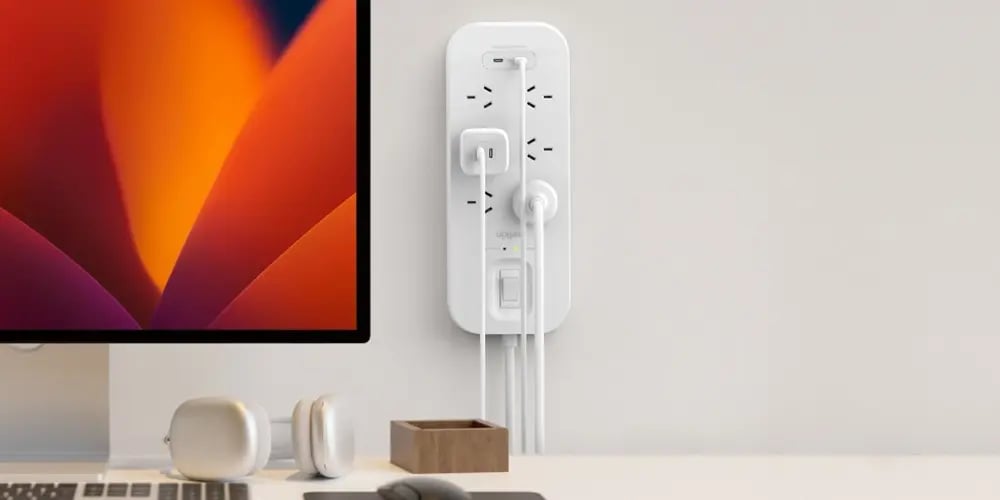 A wall-mounted power board with multiple devices plugged in beside a desktop computer.
