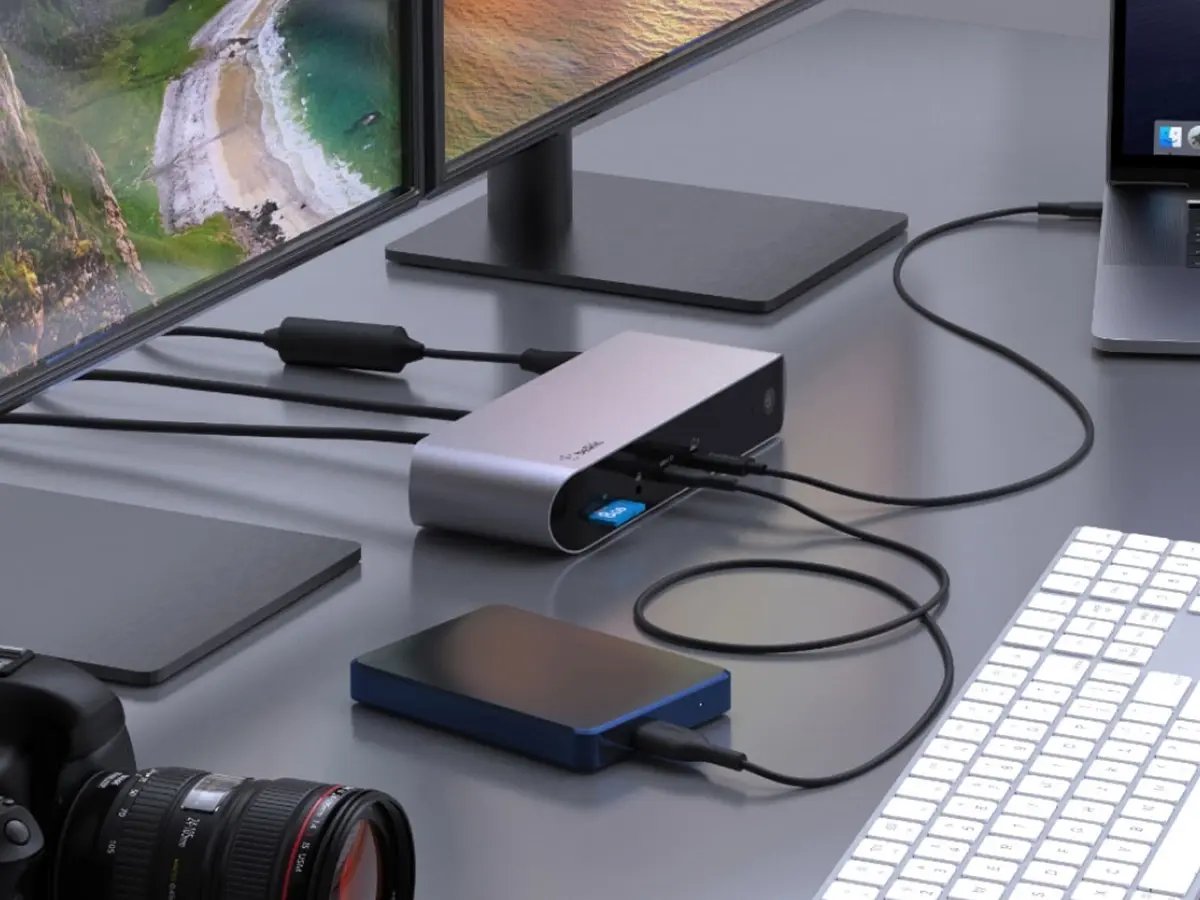 A laptop connected to a monitor through a compact docking station on a desk.