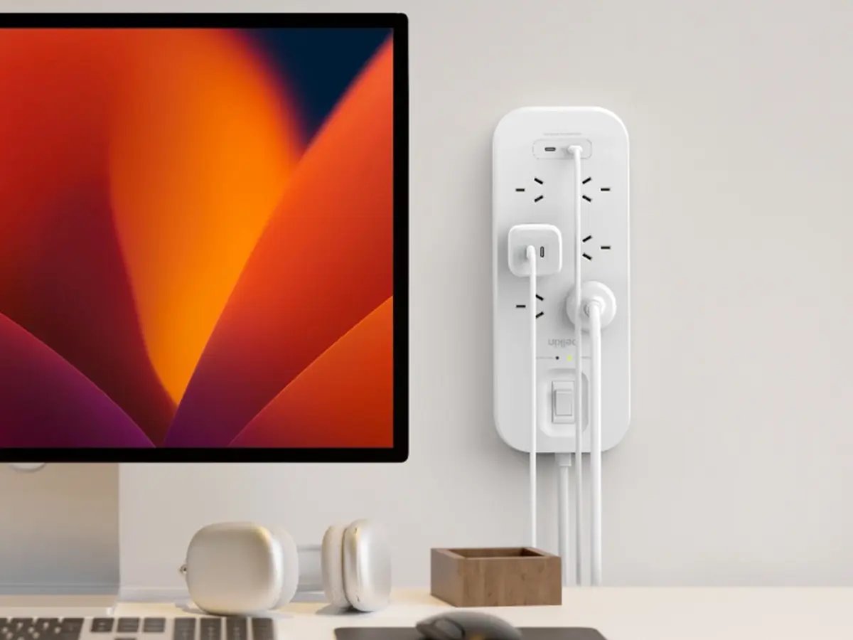 A wall-mounted power board with multiple devices plugged in beside a desktop computer.