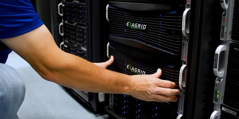 A person wearing a blue shirt adjusts a black server unit labeled 