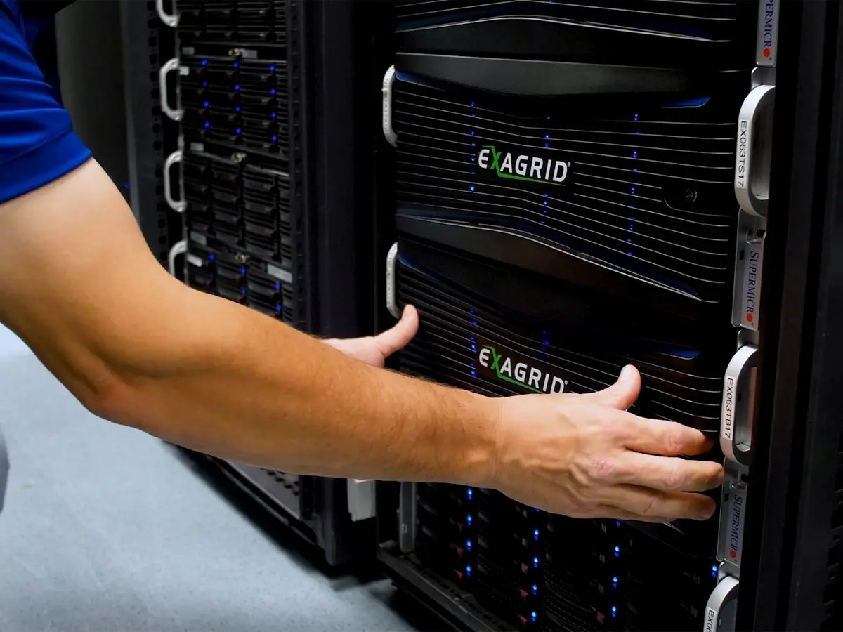 A person wearing a blue shirt adjusts a black server unit labeled 