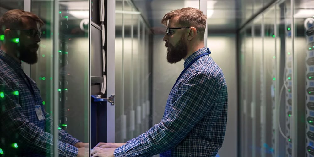 IT technician accessing a server cabinet in a data centre aisle lined with illuminated equipment racks.