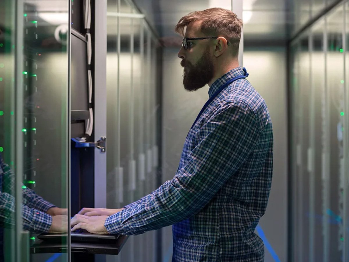 IT technician accessing a server cabinet in a data centre aisle lined with illuminated equipment racks.