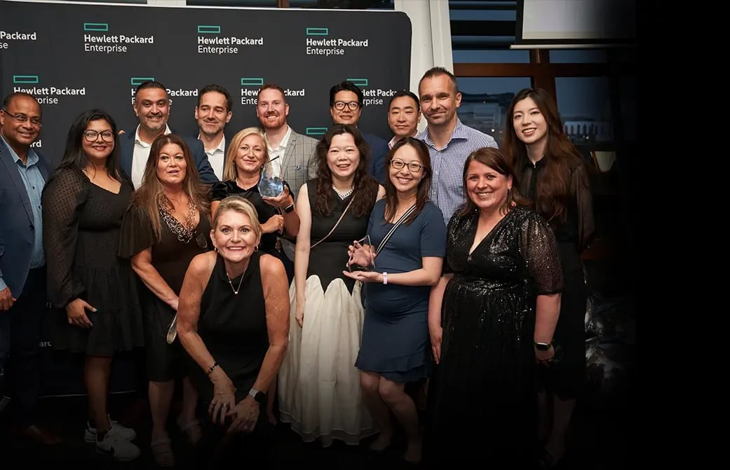 Group of people posing together at a Hewlett Packard Enterprise event with branded signage in the background.