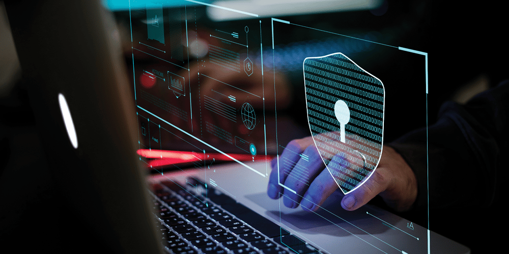Close-up of hands using a laptop keyboard with a digital cybersecurity interface overlay, including a shield icon, binary code, and virtual security panels representing data protection and network security.