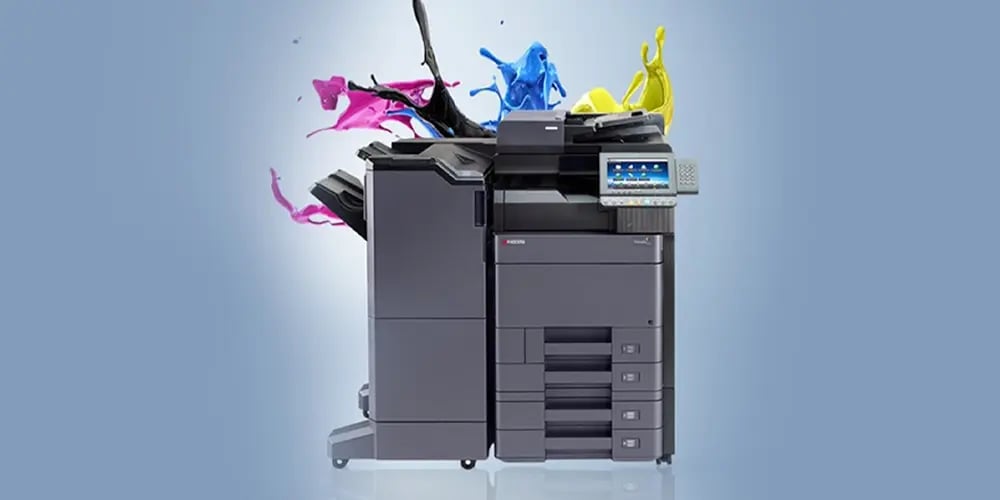 A multifunction printer with a touchscreen display. Vibrant splashes of black, magenta, cyan, and yellow ink emerge from the top, illustrating color capability.