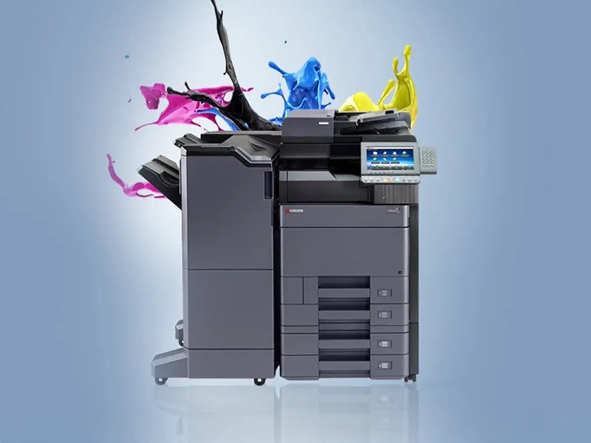 A multifunction printer with a touchscreen display. Vibrant splashes of black, magenta, cyan, and yellow ink emerge from the top, illustrating color capability.