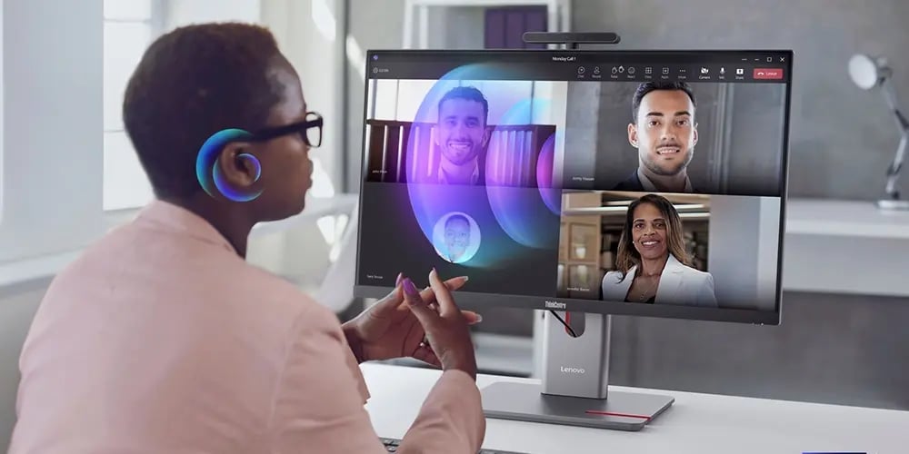 Person using a Lenovo desktop computer while participating in a video conference on a large monitor.