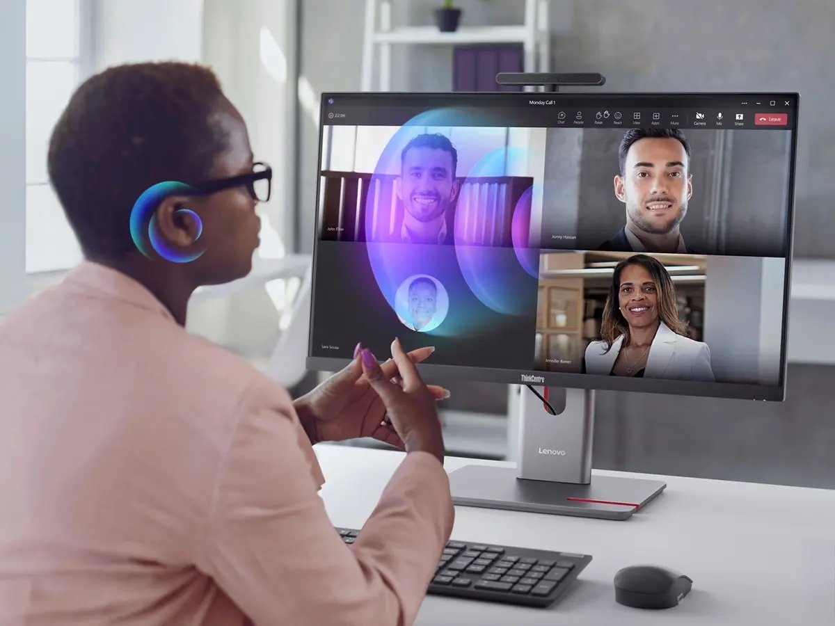Person using a Lenovo desktop computer while participating in a video conference on a large monitor.