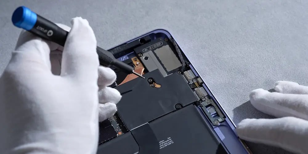 Gloved hands using a tool to repair or assemble internal components of an electronic device.