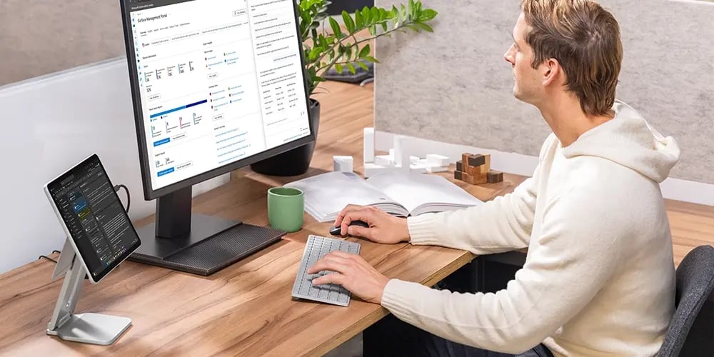 A person working at a desk with a large monitor and a Surface device on a stand.
