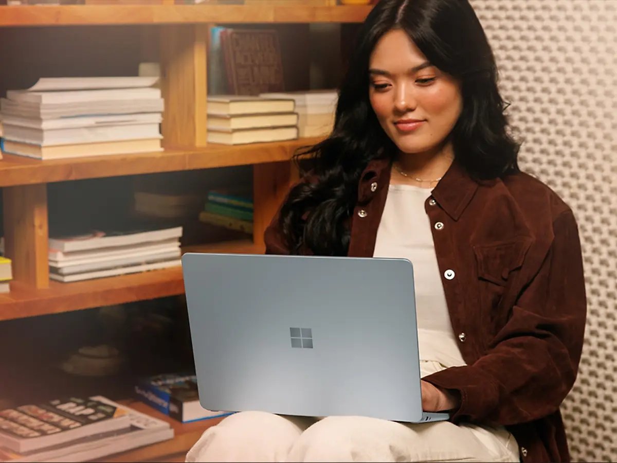A person working on a Microsoft Surface laptop while seated in front of a bookshelf.