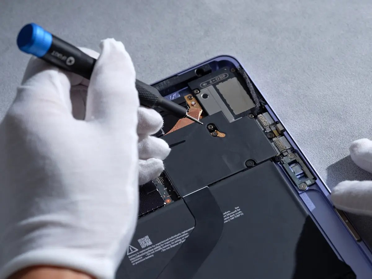 Gloved hands using a tool to repair or assemble internal components of an electronic device.