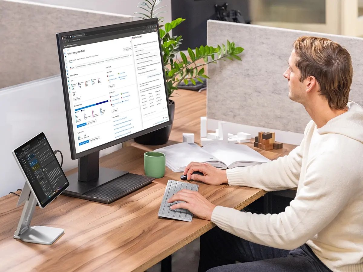 A person working at a desk with a large monitor and a Surface device on a stand.