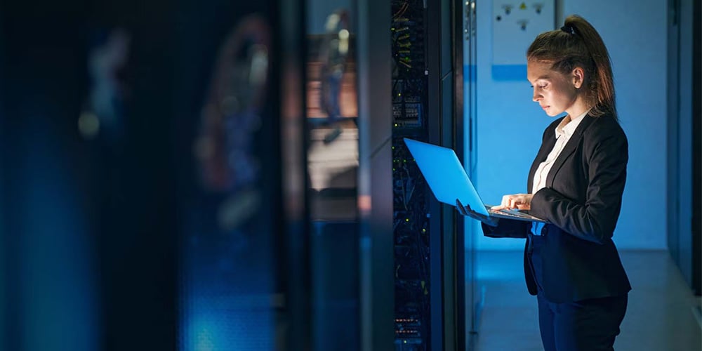 A person standing next to a server rack while working on their laptop