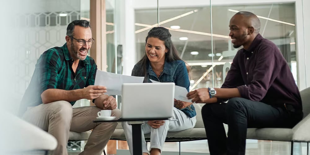 3 colleagues working together in front of a laptop and looking at documents