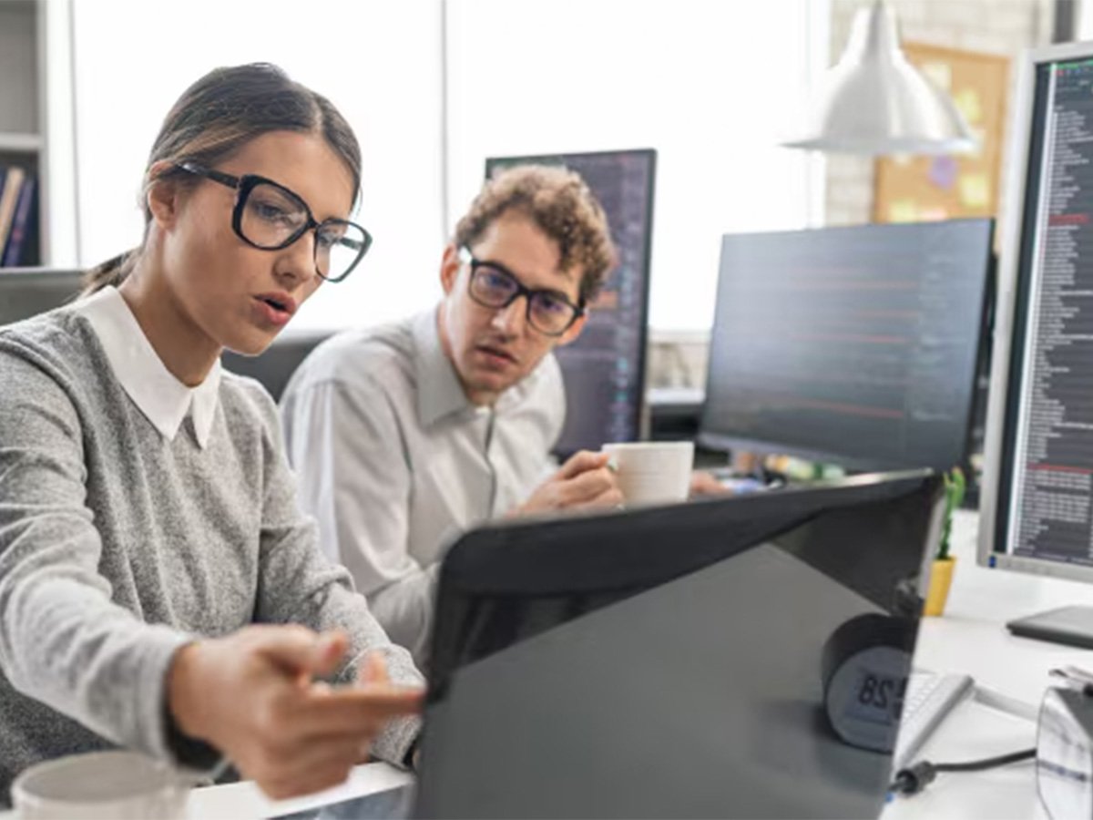 Two colleagues collaborating at a desk, reviewing information on a large monitor in an office.