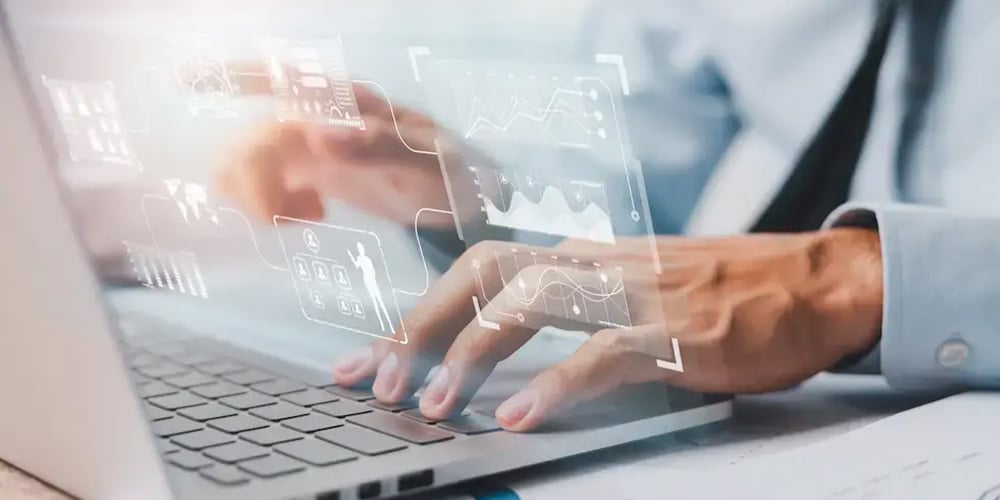 Hands typing on a laptop with transparent data charts and user interface elements overlaid.