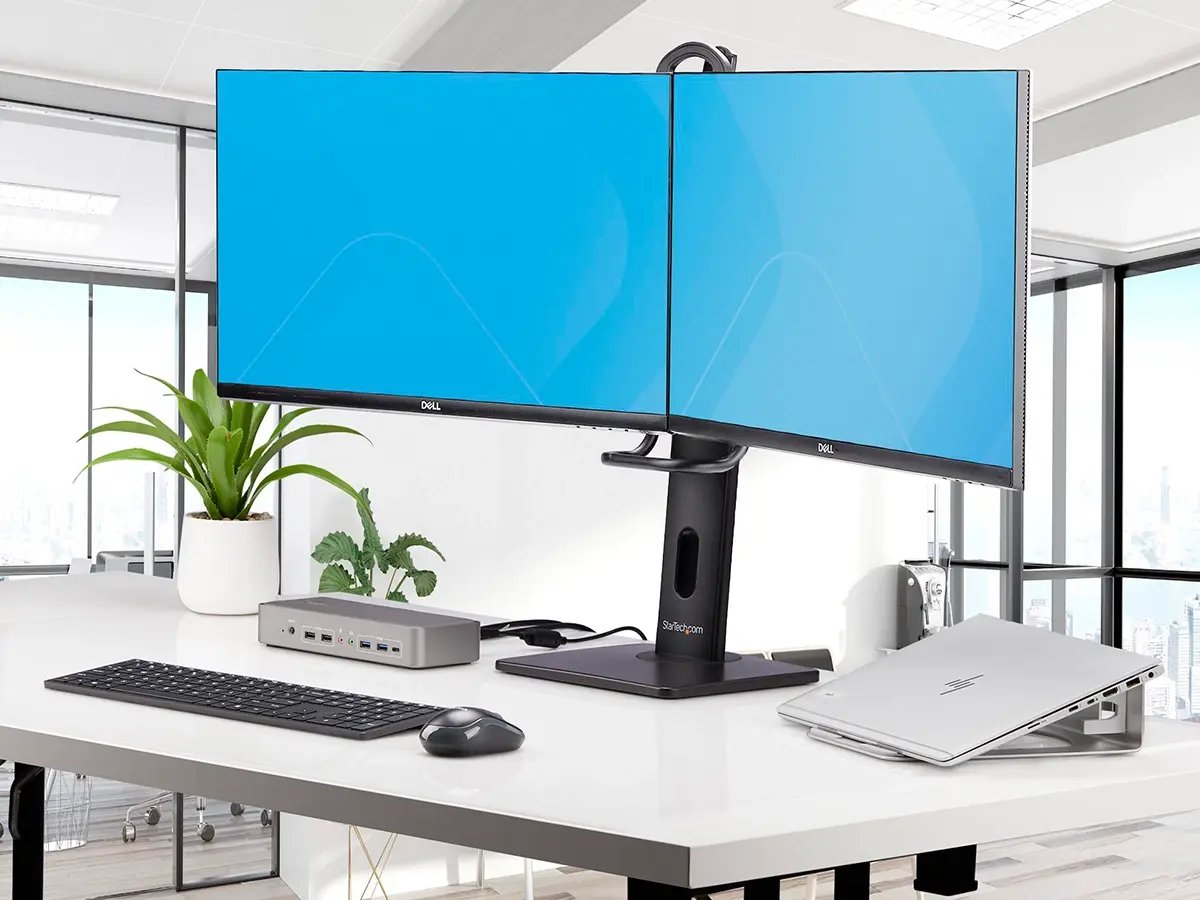 A clean workstation featuring dual Dell monitors, a StarTech docking station, keyboard, mouse, and laptop stand.