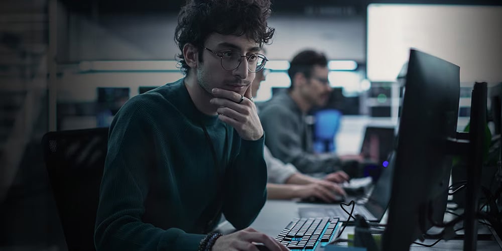 Person working on a desktop computer in a dimly lit office with multiple monitors visible.