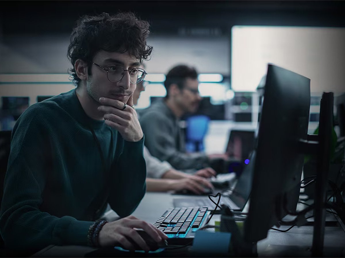 Person working on a desktop computer in a dimly lit office with multiple monitors visible.