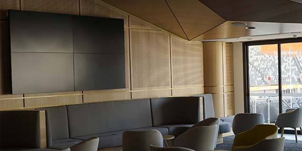 Contemporary lounge area with cushioned chairs, a wall-mounted screen, and natural light from glass doors.